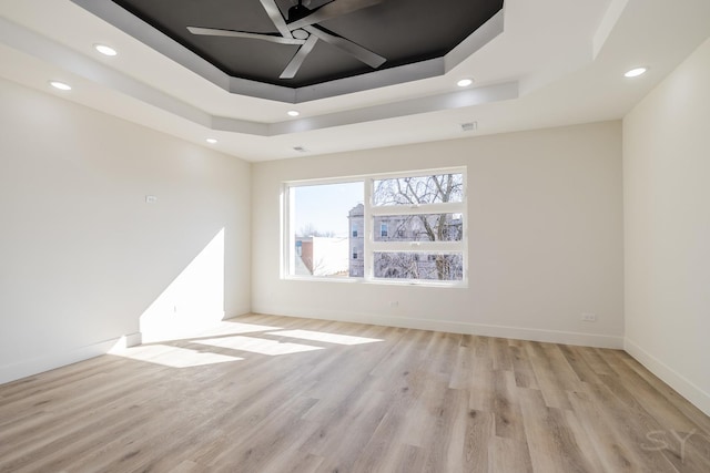 spare room with light wood-style flooring, a raised ceiling, and ceiling fan