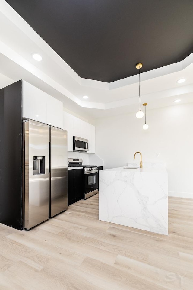 kitchen featuring decorative light fixtures, white cabinetry, stainless steel appliances, light wood-style floors, and a raised ceiling