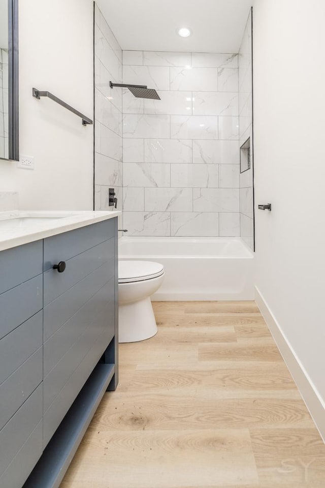 bathroom featuring baseboards, toilet, shower / bathtub combination, wood finished floors, and vanity