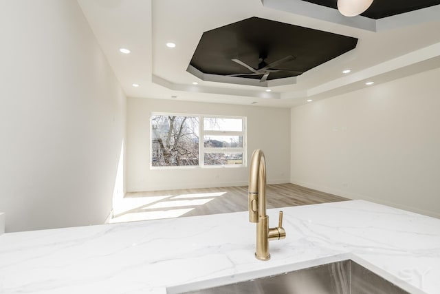 interior details featuring light stone countertops, a tray ceiling, recessed lighting, wood finished floors, and a sink