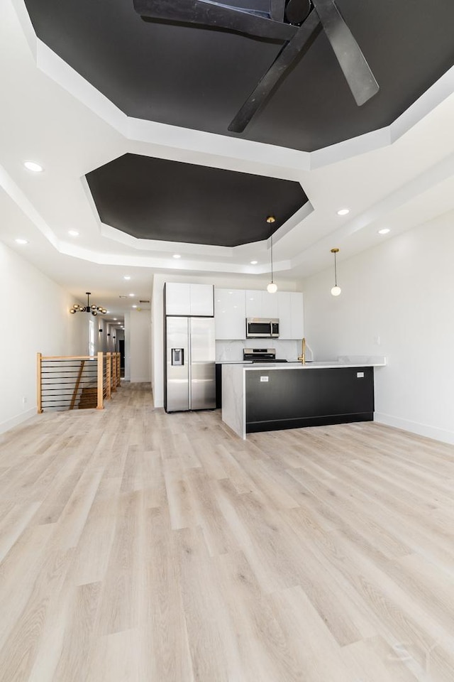 kitchen featuring white cabinetry, stainless steel appliances, light wood-type flooring, and a tray ceiling