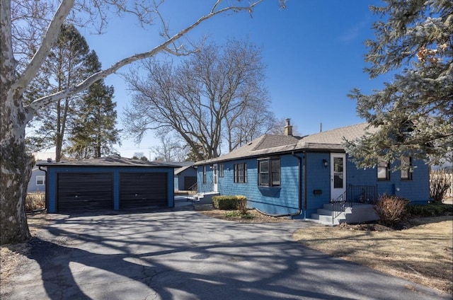 ranch-style home with a garage, an outbuilding, roof with shingles, and a chimney