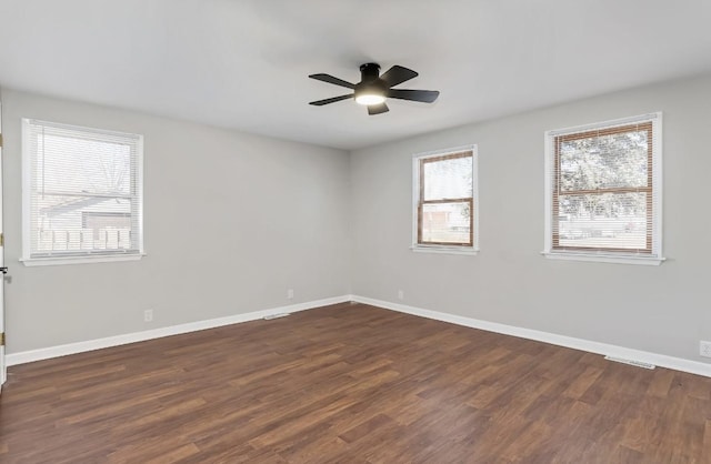 spare room featuring ceiling fan, visible vents, baseboards, and dark wood finished floors