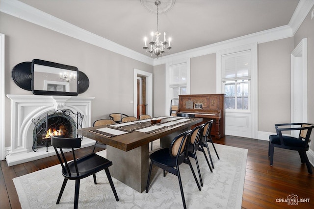 dining area featuring crown molding, wood-type flooring, a chandelier, and a lit fireplace