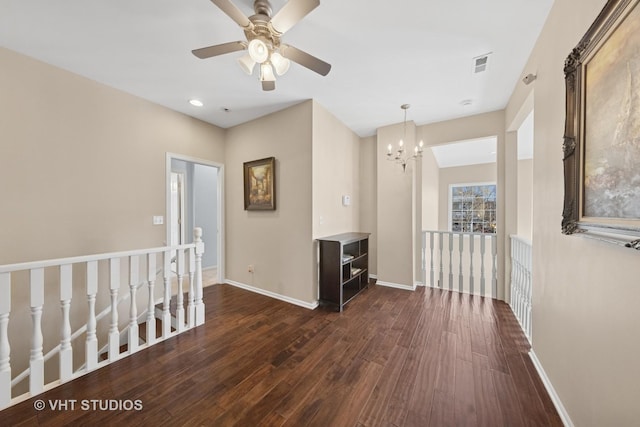 empty room featuring dark wood finished floors, ceiling fan with notable chandelier, baseboards, and visible vents