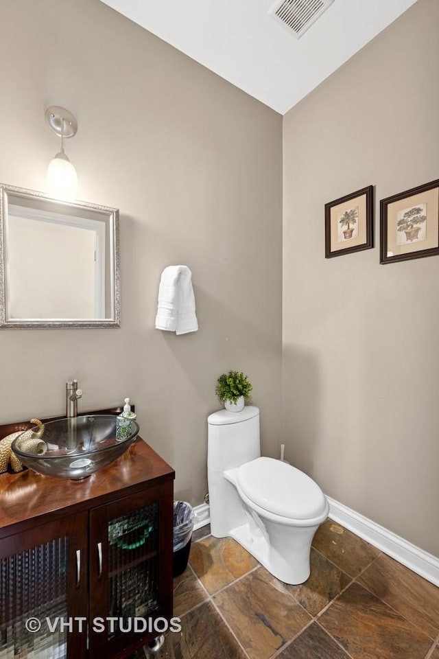 bathroom featuring vanity, baseboards, visible vents, stone finish floor, and toilet