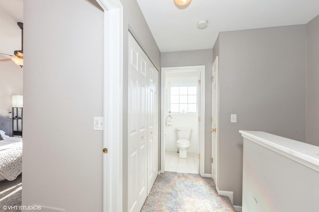 hall with light tile patterned floors, baseboards, and light carpet