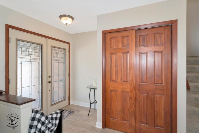 foyer featuring baseboards, light wood-style flooring, and stairs