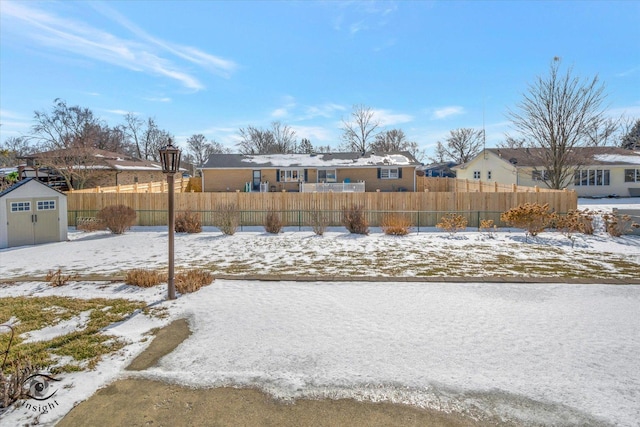 snowy yard with a fenced front yard, a shed, a residential view, and an outdoor structure