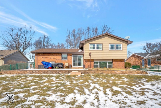 snow covered back of property with brick siding and fence