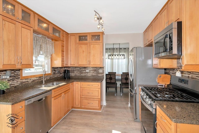 kitchen featuring a sink, tasteful backsplash, stainless steel appliances, dark stone counters, and light wood finished floors