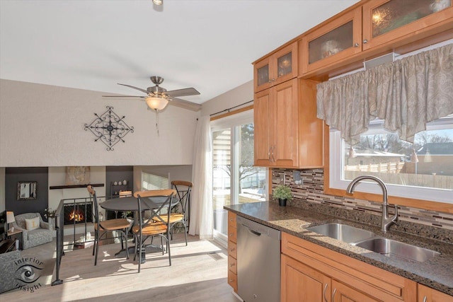 kitchen with dark stone countertops, a warm lit fireplace, a sink, dishwasher, and backsplash