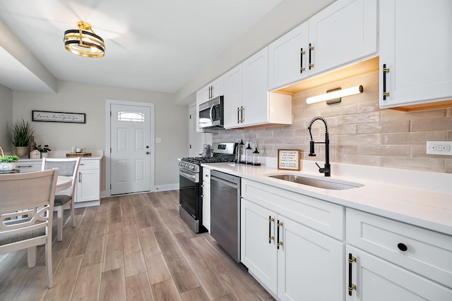 kitchen with a sink, light wood-style floors, appliances with stainless steel finishes, white cabinets, and decorative backsplash