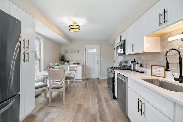 kitchen with light wood-style flooring, a sink, stainless steel appliances, light countertops, and decorative backsplash