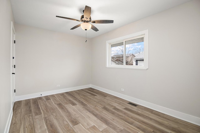 empty room featuring a ceiling fan, wood finished floors, visible vents, and baseboards