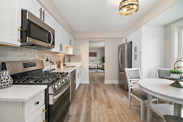 kitchen with a sink, backsplash, stainless steel appliances, white cabinets, and light wood finished floors