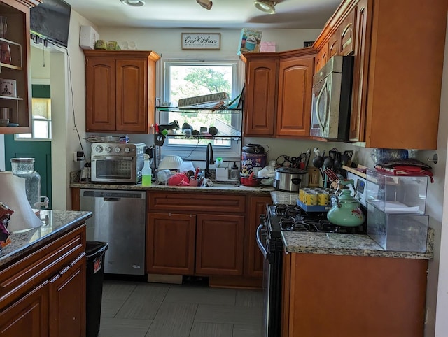 kitchen featuring a sink, stainless steel appliances, brown cabinets, and dark stone countertops