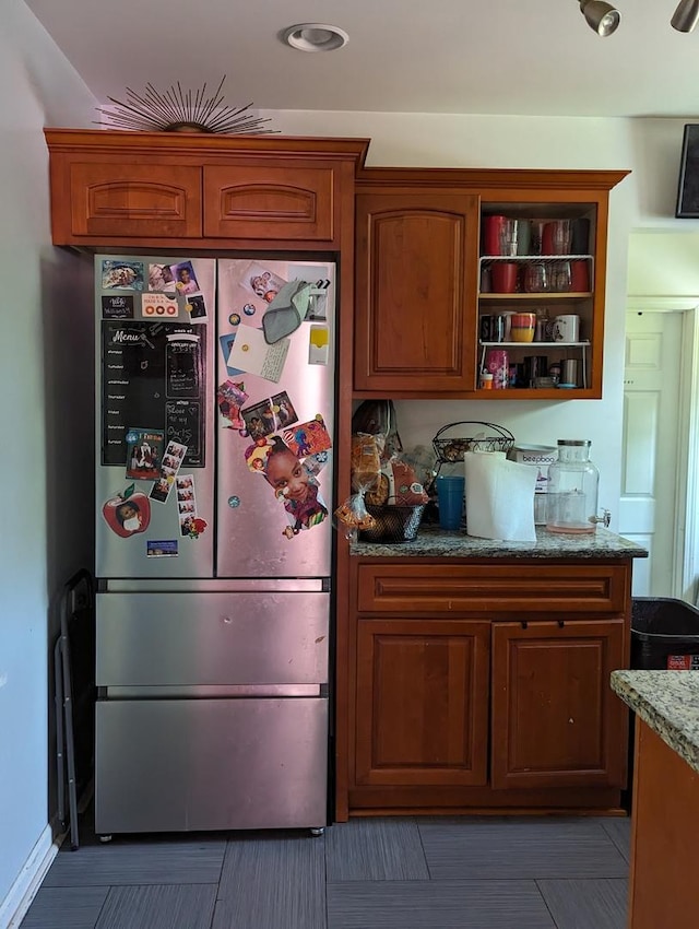 kitchen featuring brown cabinetry, stone countertops, freestanding refrigerator, and open shelves