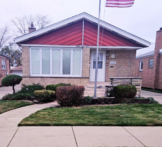 view of front facade with brick siding, a chimney, and a front lawn