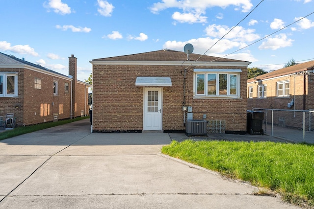 rear view of house featuring brick siding, central AC, and fence