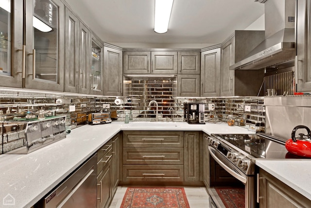 kitchen with tasteful backsplash, light countertops, stainless steel appliances, wall chimney exhaust hood, and a sink