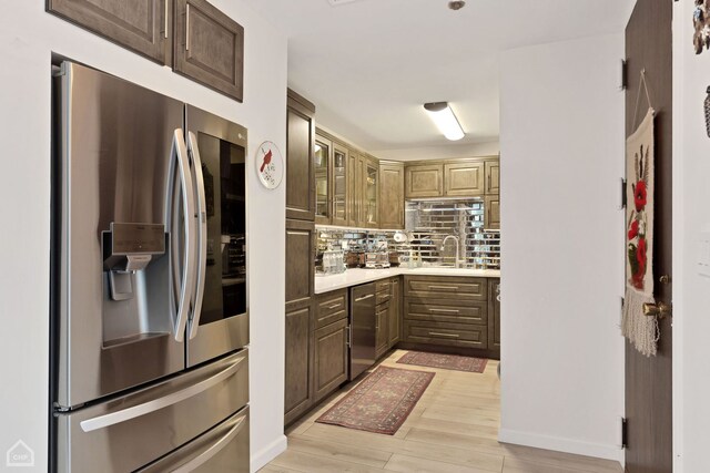 kitchen with a sink, stainless steel appliances, light countertops, light wood-style floors, and backsplash