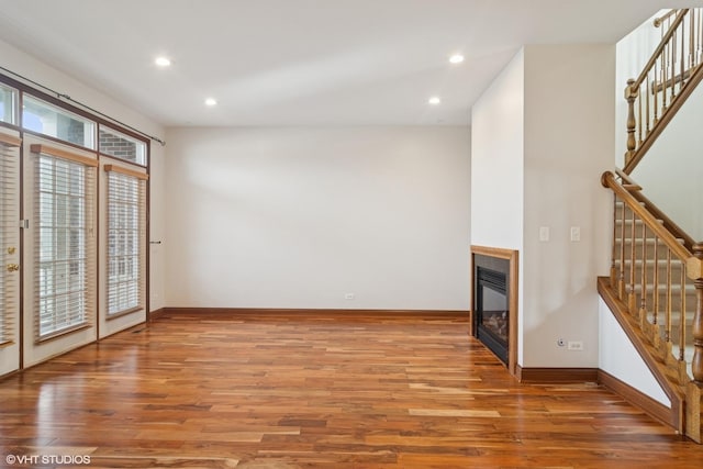 unfurnished living room with a glass covered fireplace, stairway, baseboards, and wood finished floors