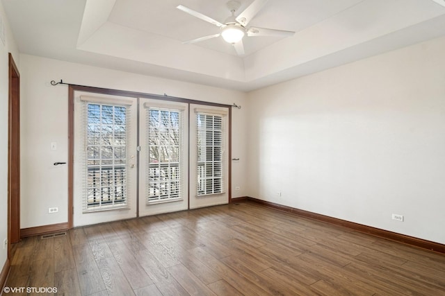 spare room with a raised ceiling, wood finished floors, visible vents, and baseboards