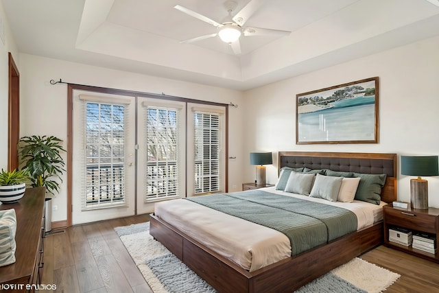 bedroom with access to exterior, a raised ceiling, a ceiling fan, and wood-type flooring