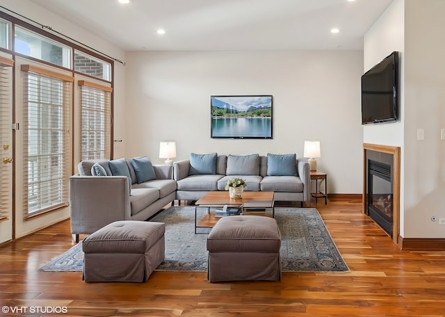 living room featuring a glass covered fireplace, baseboards, wood finished floors, and recessed lighting