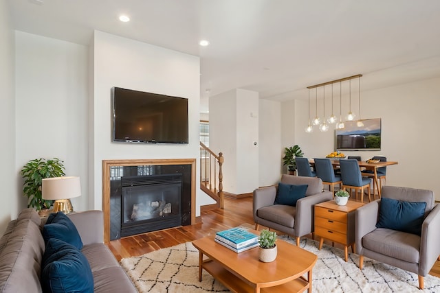 living area featuring a glass covered fireplace, recessed lighting, baseboards, and wood finished floors