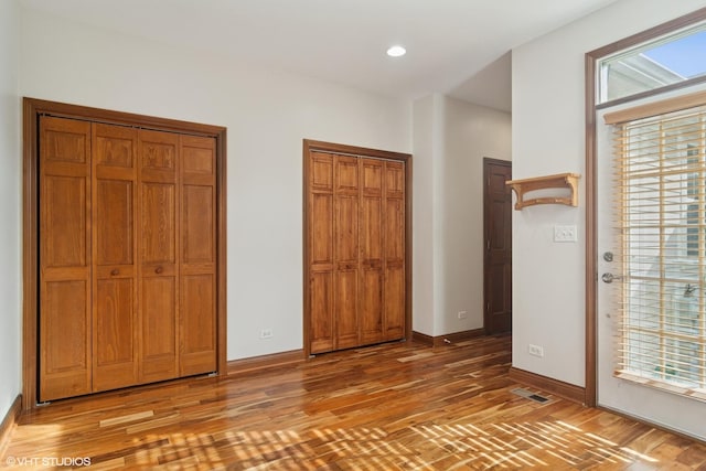 unfurnished bedroom with visible vents, light wood-style flooring, multiple closets, and multiple windows