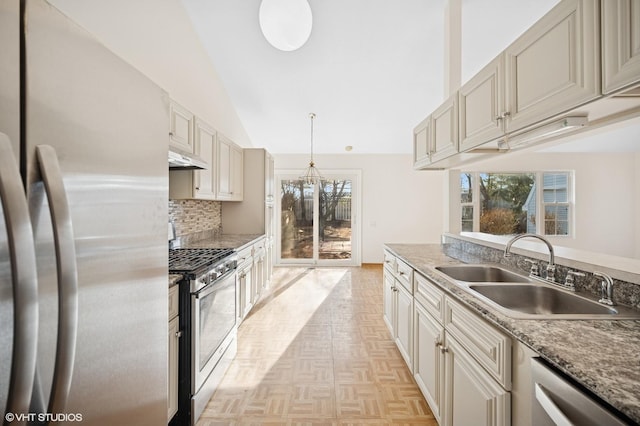 kitchen with vaulted ceiling, decorative backsplash, appliances with stainless steel finishes, cream cabinetry, and a sink