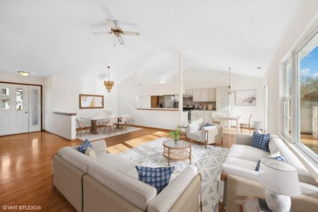 living area with ceiling fan with notable chandelier, light wood-style flooring, and vaulted ceiling