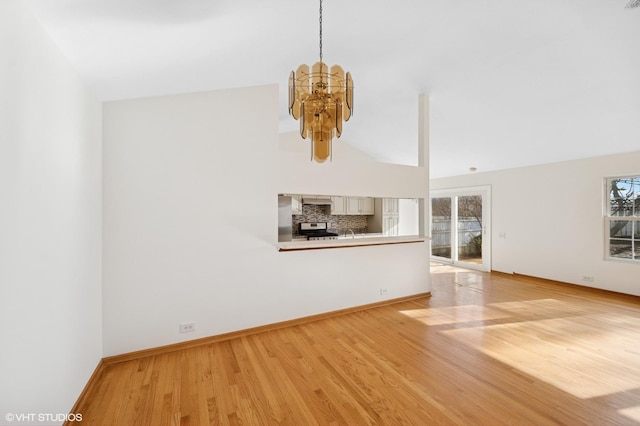 unfurnished living room featuring a notable chandelier, plenty of natural light, baseboards, and light wood finished floors