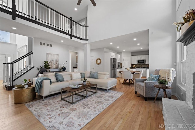 living area with visible vents, a towering ceiling, stairs, and light wood finished floors