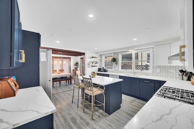 kitchen featuring tasteful backsplash, blue cabinetry, ventilation hood, a breakfast bar area, and light stone counters