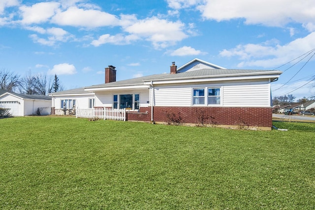 back of house featuring fence, a chimney, a detached garage, a lawn, and brick siding