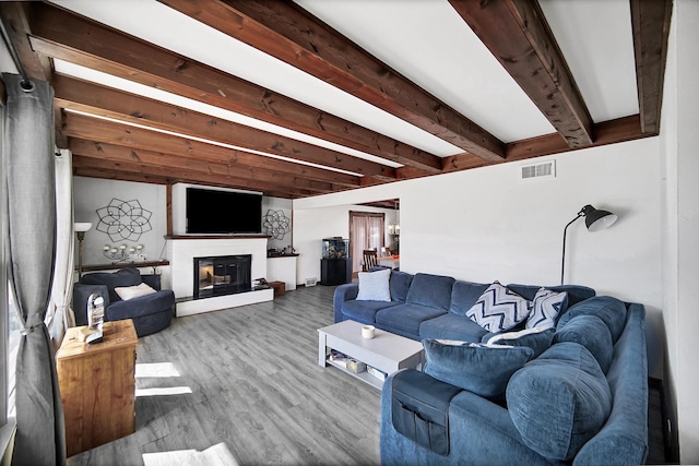 living area featuring wood finished floors, visible vents, beam ceiling, and a glass covered fireplace