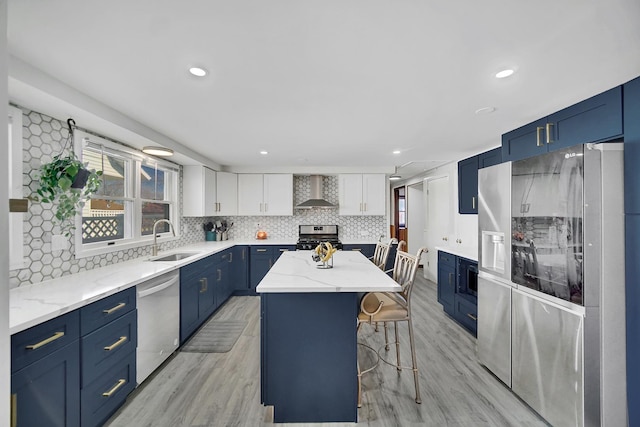 kitchen with a sink, blue cabinetry, a kitchen island, stainless steel appliances, and wall chimney range hood