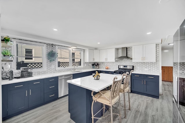 kitchen featuring a breakfast bar area, blue cabinets, appliances with stainless steel finishes, white cabinetry, and wall chimney exhaust hood