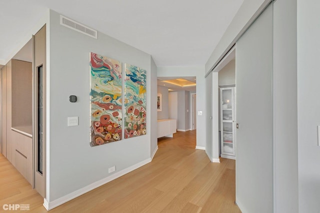 hall with light wood-style flooring, baseboards, and visible vents