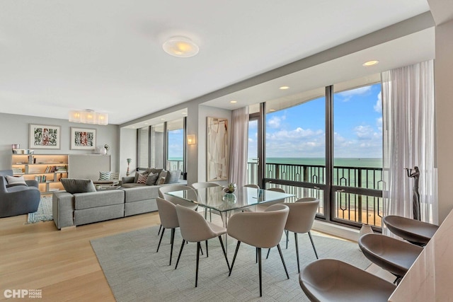 dining room with a wall of windows, light wood-type flooring, and a water view