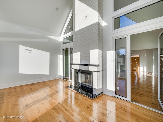 unfurnished living room with baseboards, high vaulted ceiling, hardwood / wood-style floors, and a fireplace