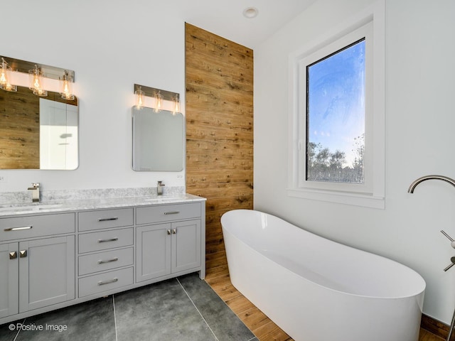 full bath with double vanity, wood finished floors, a freestanding bath, and a sink