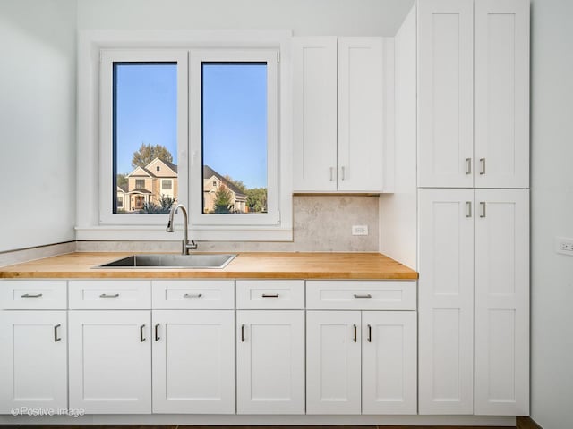 kitchen with butcher block countertops, white cabinetry, and a sink