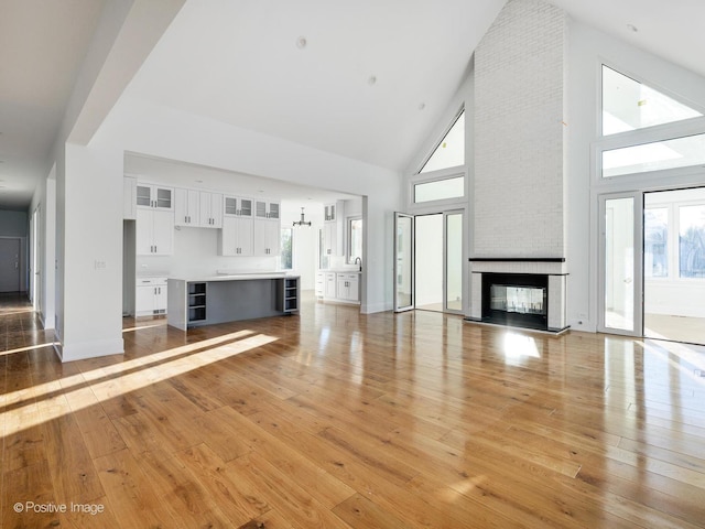 unfurnished living room featuring a brick fireplace, a healthy amount of sunlight, light wood finished floors, and high vaulted ceiling