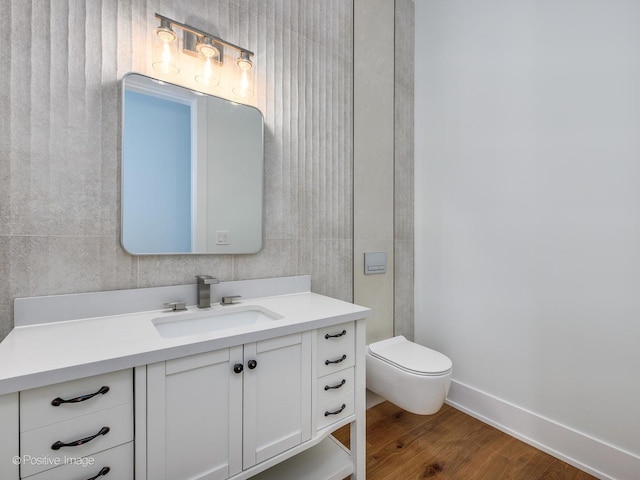 bathroom with toilet, vanity, baseboards, and wood finished floors