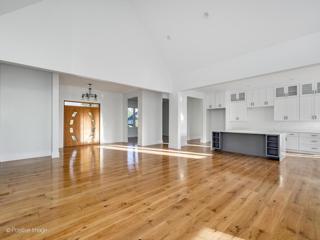 unfurnished living room with light wood finished floors, a chandelier, and high vaulted ceiling