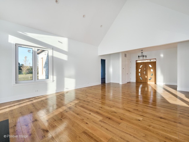 unfurnished living room with high vaulted ceiling, light wood-type flooring, and baseboards